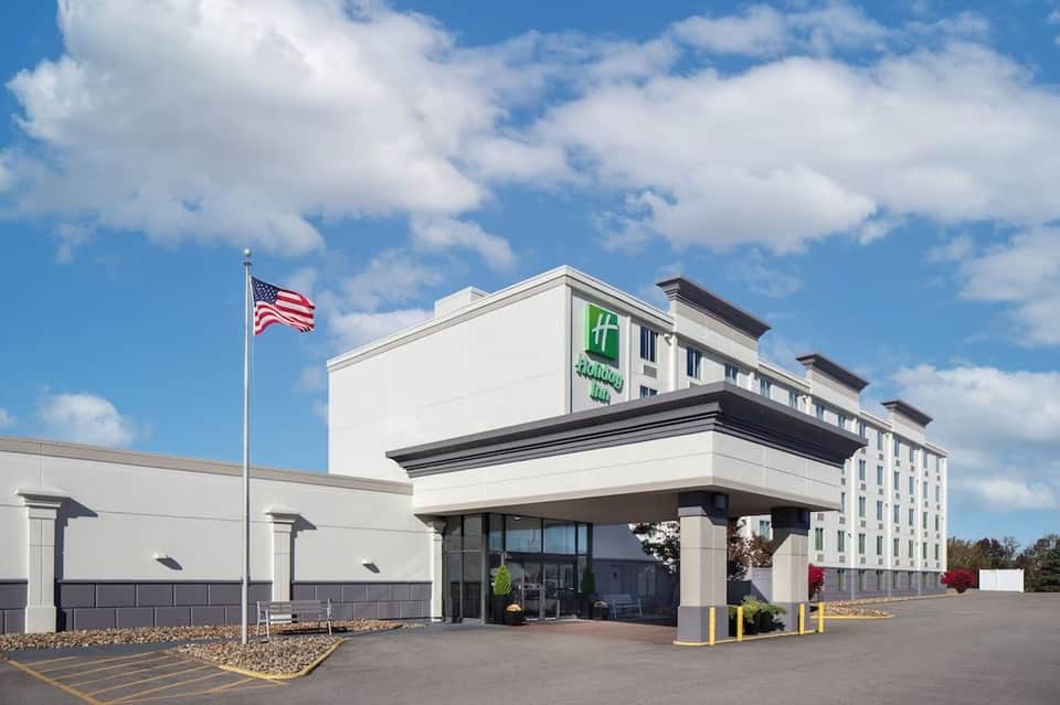 Holiday Inn hotel exterior with white facade, American flag, and parked cars