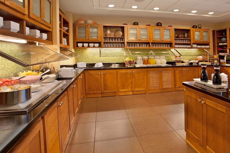 Large hotel kitchen with golden wood cabinetry, green tile backsplash, stainless steel appliances, and full food service setup