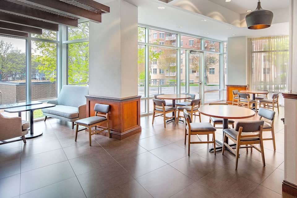 Modern hotel lounge with wood tables, blue chairs, large windows overlooking city street