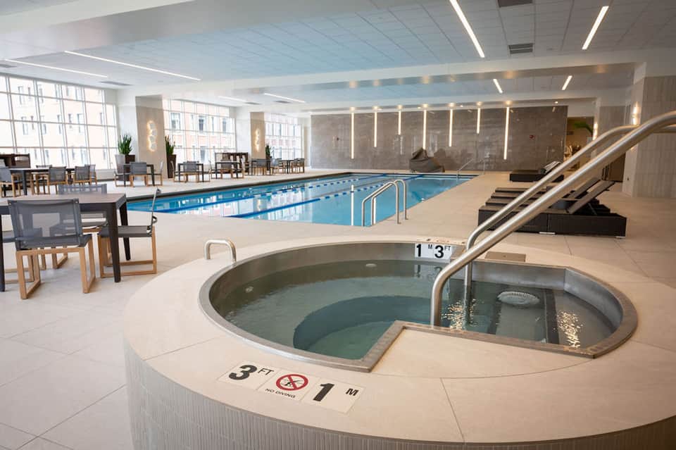Indoor pool and hot tub facility with lap pool, spa tub, lounge chairs, and bright lighting