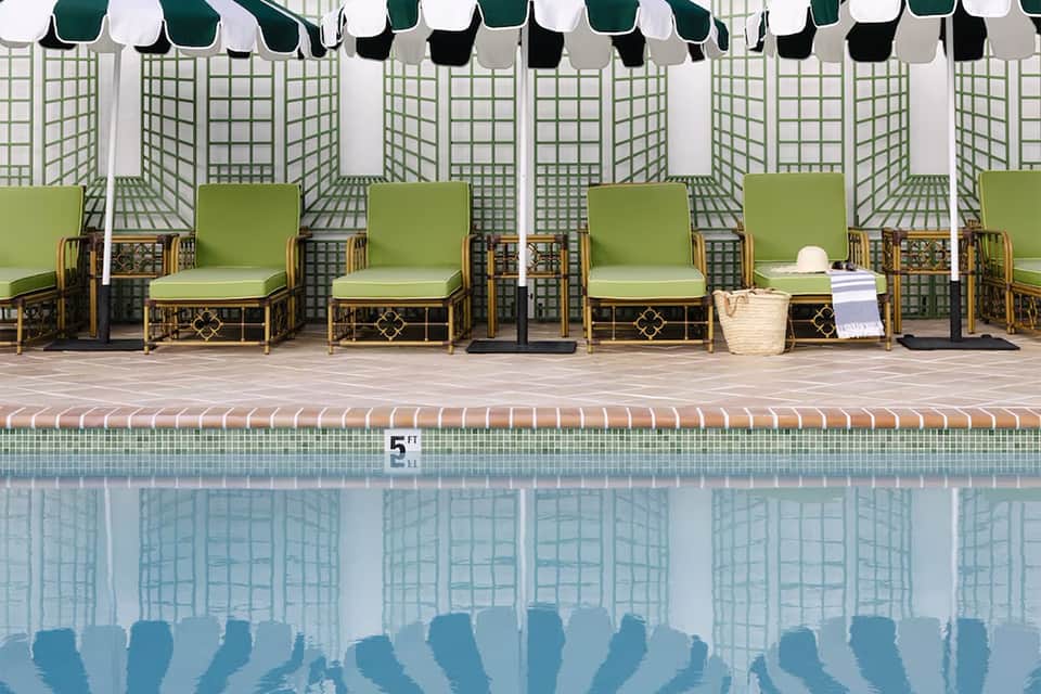 Resort pool with green lounge chairs under striped umbrellas and lattice privacy screens