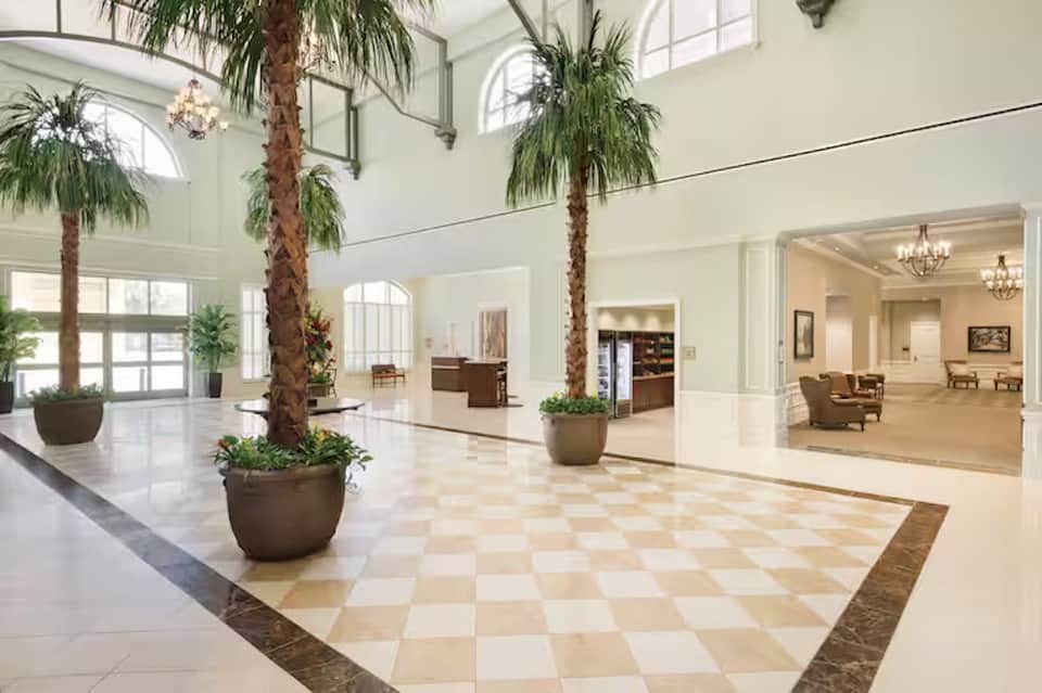 Grand hotel lobby with soaring ceilings, tall palm trees in planters, and checkered marble flooring
