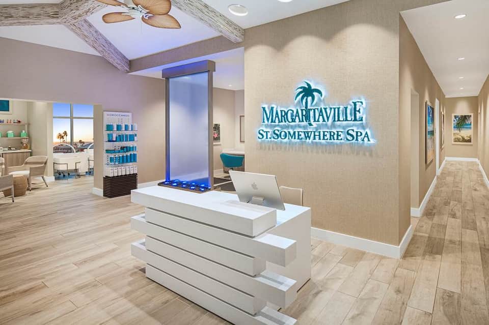 Spa reception area with Margaritaville St. Somewhere Spa branding, modern desk, and blue water feature