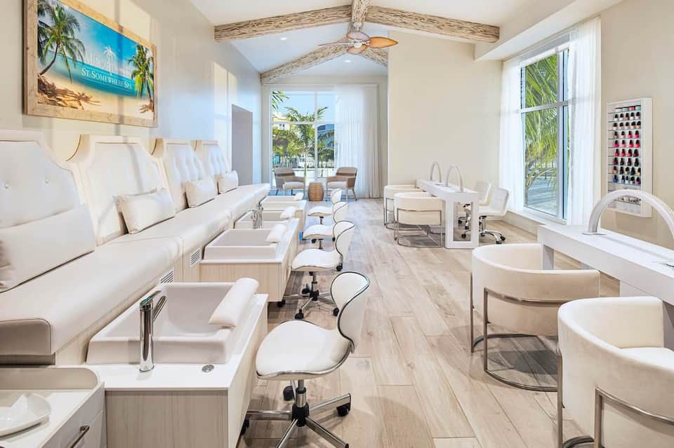 Bright spa interior with nail stations, pedicure chairs, and ocean views through floor-to-ceiling windows