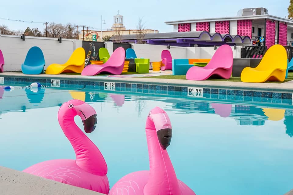 Colorful pool with pink flamingo floats, neon-colored loungers, and vibrant poolside decor