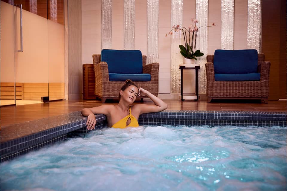 Woman in yellow bikini relaxing in indoor hot tub with modern furniture and ambient lighting