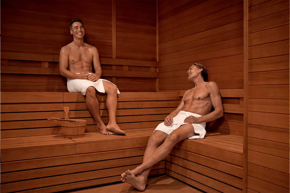 Two men relaxing in wooden sauna with benches and traditional sauna bucket