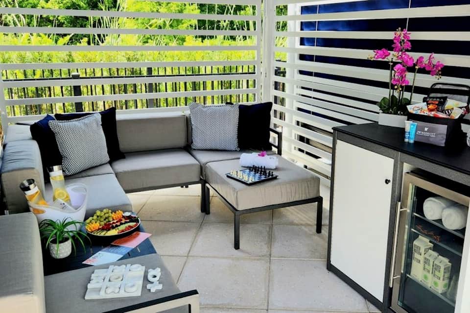 Modern outdoor lounge with gray sectional sofa, striped privacy screens, and potted orchid flowers