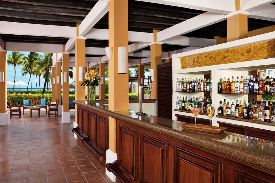Tropical bar interior with wooden columns, palm trees, ocean views, and full liquor selection
