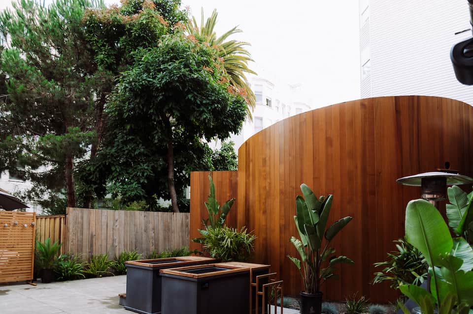 Modern patio with curved wooden accent wall, fire pit, tropical plants, and contemporary architectural design