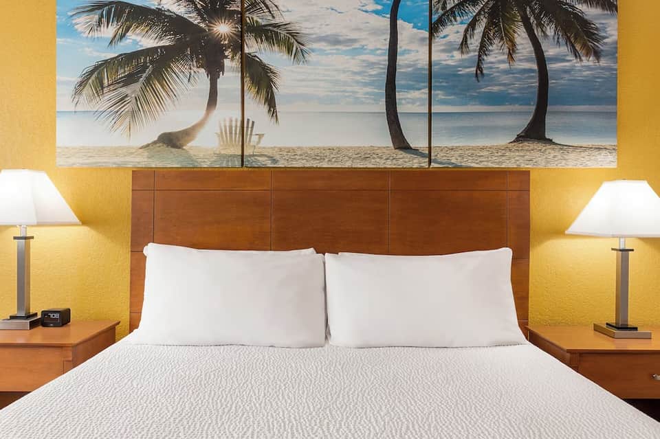 Hotel bedroom with yellow accent walls, wooden headboard, and tropical beach wall art
