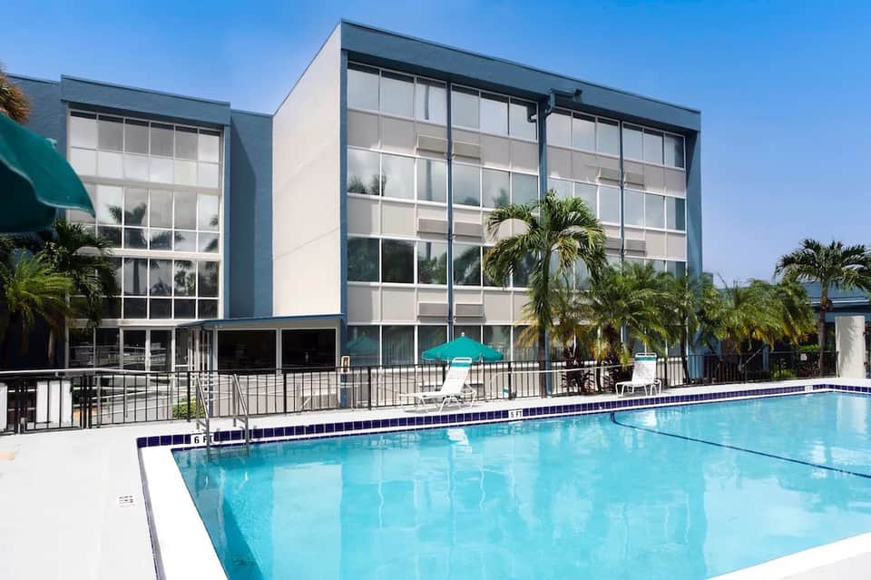 Modern hotel building with glass facade next to sparkling blue pool and tropical palm trees