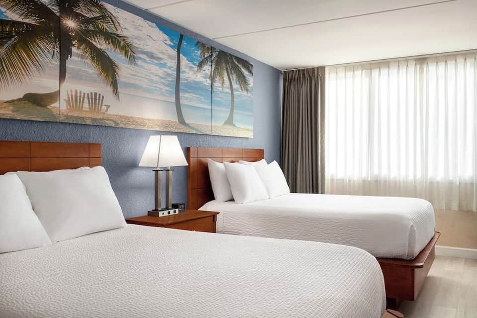 Hotel room with two queen beds, beach-themed wall art, and curtained windows