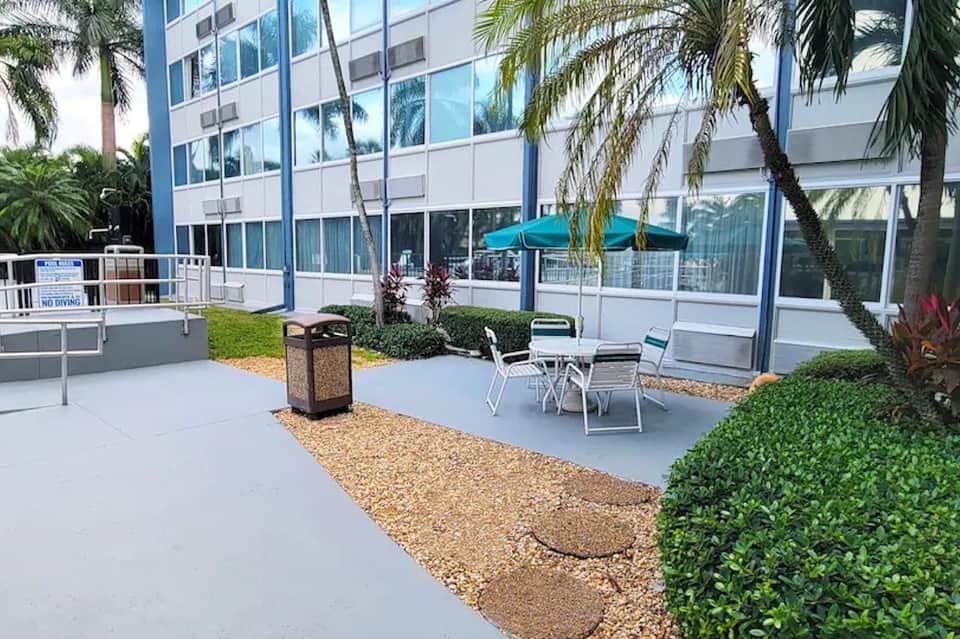 Modern outdoor patio with turquoise umbrella, seating, and contemporary building exterior with palms