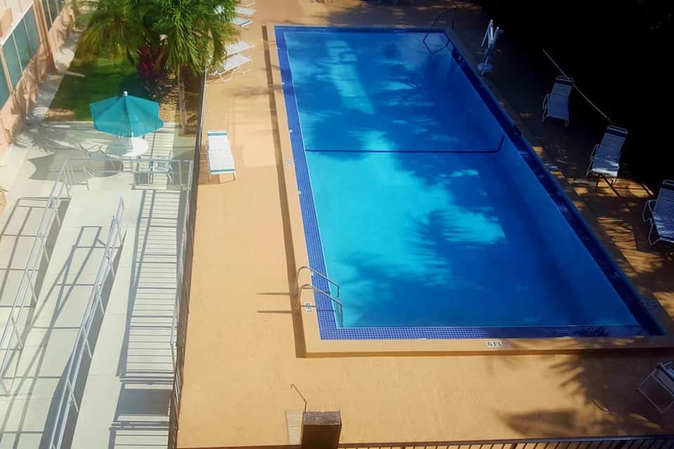 Aerial view of rectangular swimming pool with blue water, lounge chairs, and palm trees on concrete deck
