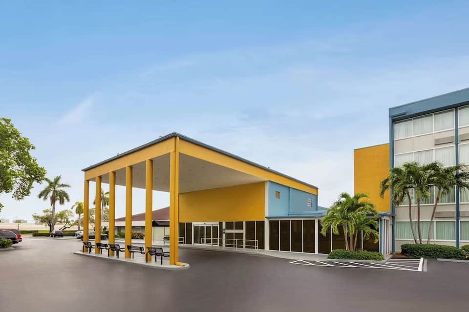 Contemporary hotel entrance with bright yellow canopy, palm trees, and geometric architecture