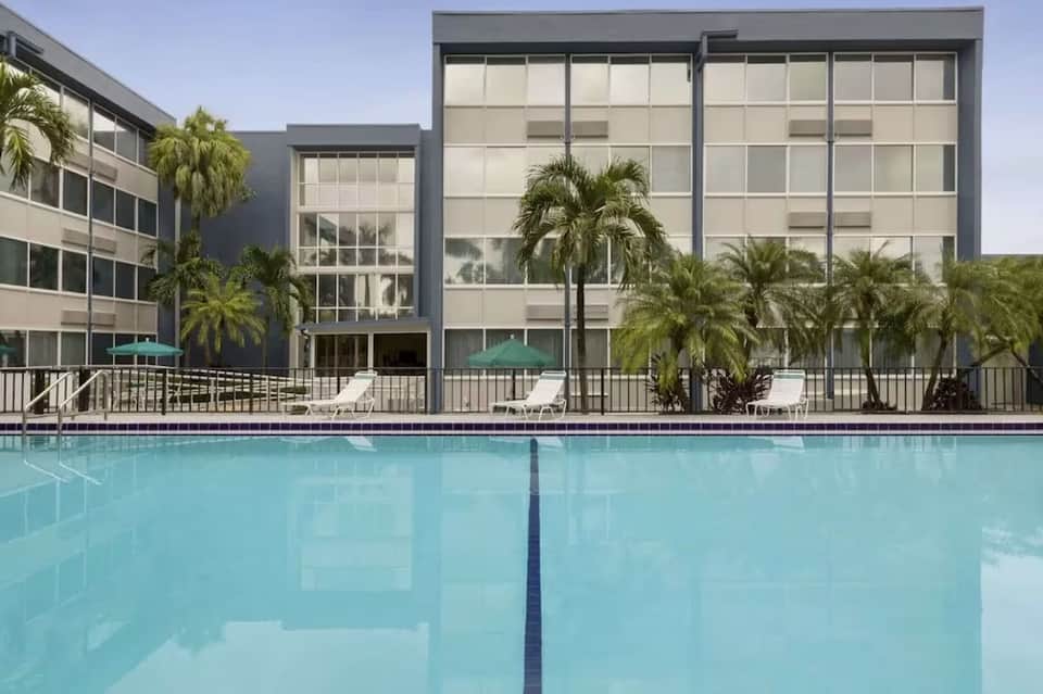 Modern hotel pool with lap lanes, palm trees, multi-story building facade with grid windows
