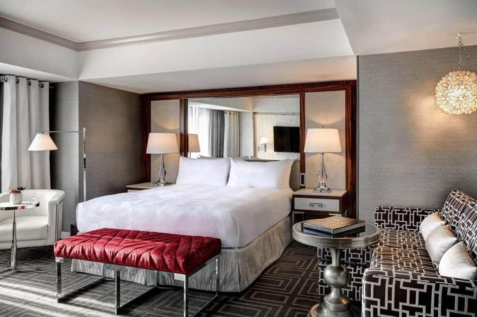 Luxurious hotel bedroom with white bedding, mirrored headboard, red bench, and contemporary furnishings
