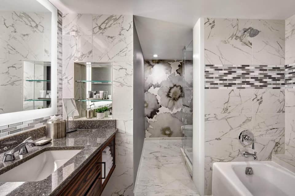 Marble bathroom with dual vanity sink, large mirror, walk-in shower, and white tub