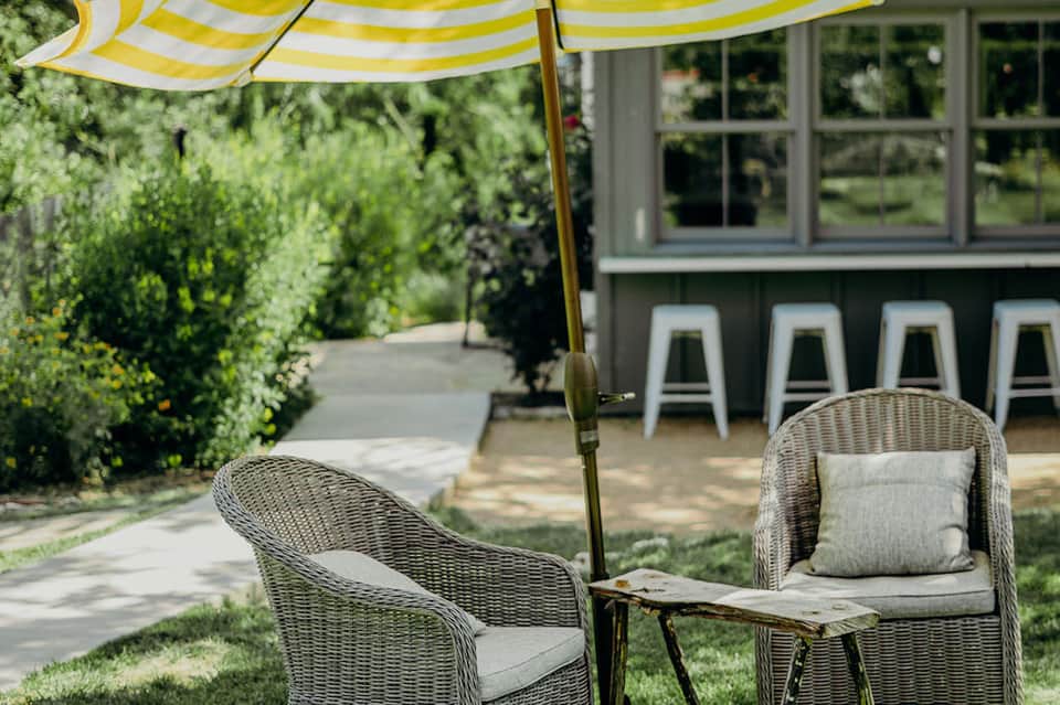 Outdoor patio seating area with wicker chairs under striped yellow and white umbrella