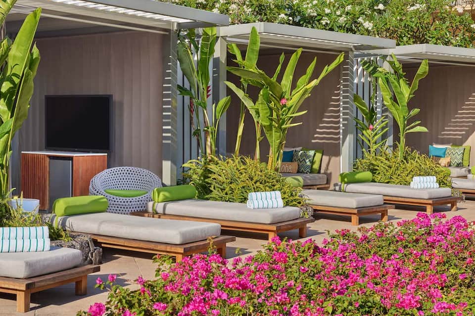 Outdoor lounge area with wooden daybeds, magenta flowers, and shaded pergolas near spa