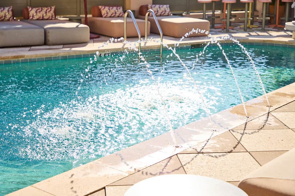Resort pool with fountain features, lounge seating, and sunny courtyard area