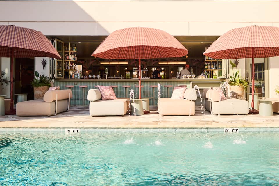 Resort poolside lounge with curved cream seating, red umbrellas, tiled bar, and crystal-clear water