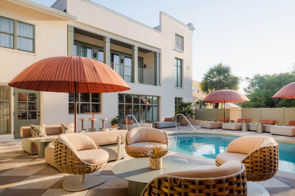 Outdoor pool area with loungers, red umbrellas, wicker seating, and modern architecture