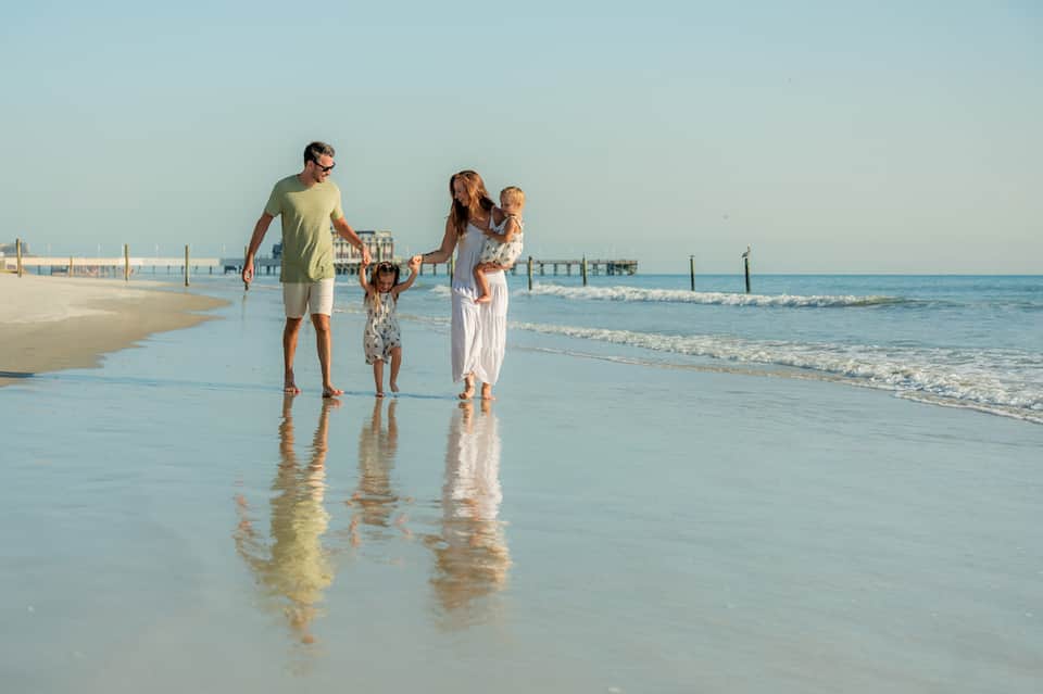 Family wading in shallow ocean water with pier visible in background