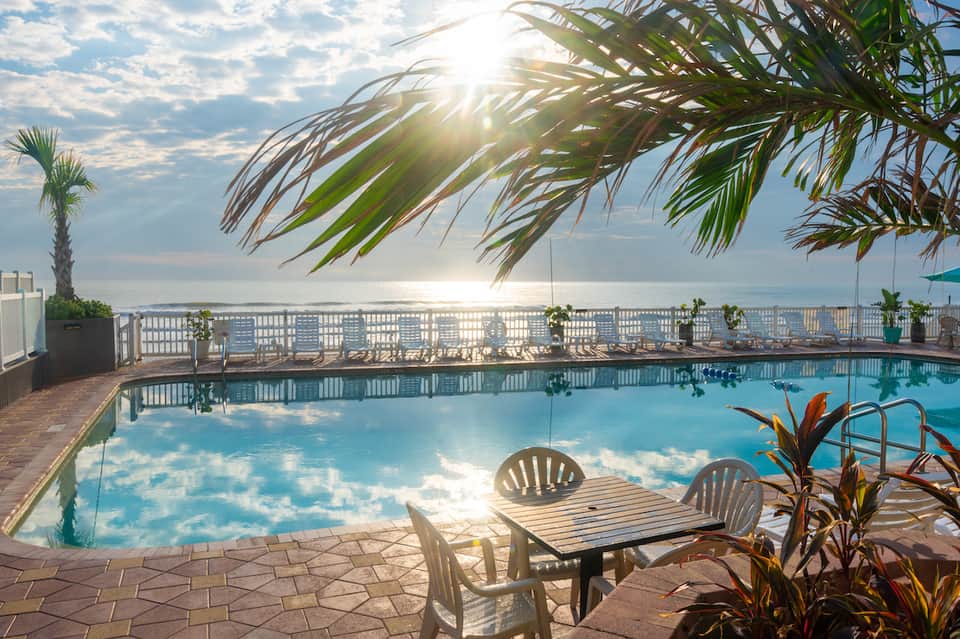 Oceanfront pool deck with lounge chairs, white railing, palm fronds, and serene water view