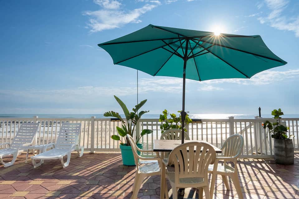 Beachfront deck with white loungers, turquoise umbrella, ocean view, and white railing