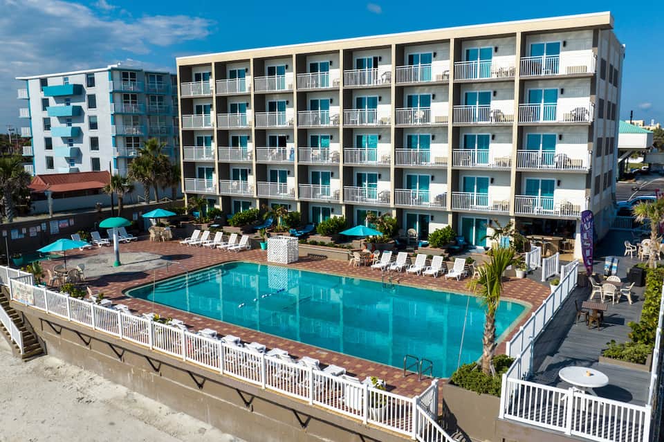 Beachfront hotel building with turquoise pool, white umbrellas, and palm trees