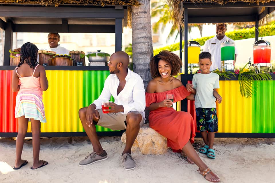 Family enjoying colorful beach bar with red, yellow, and green corrugated metal design and palm trees