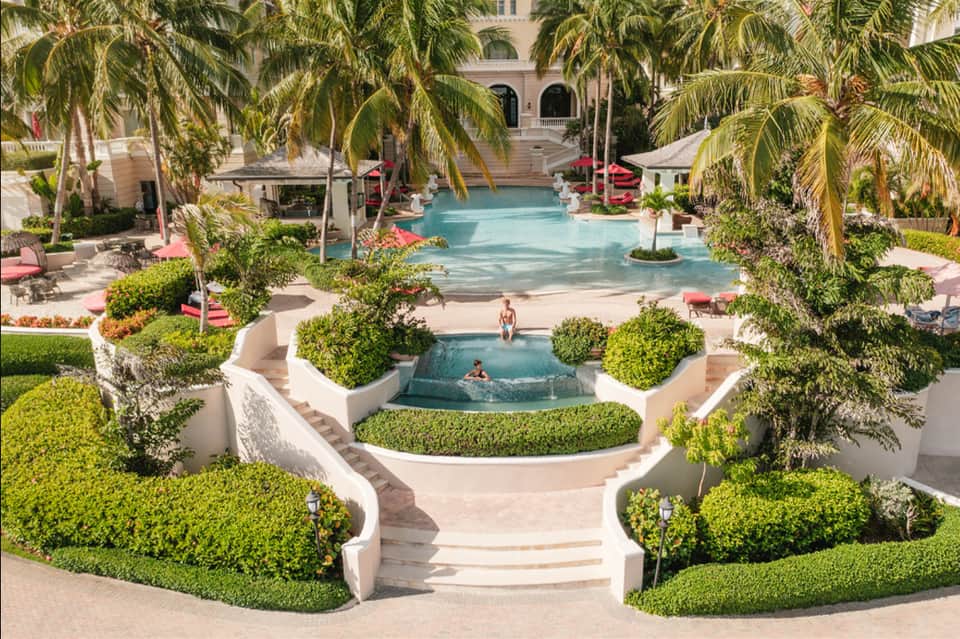 Luxurious courtyard with tiered pools, palm trees, manicured hedges, and beige architecture