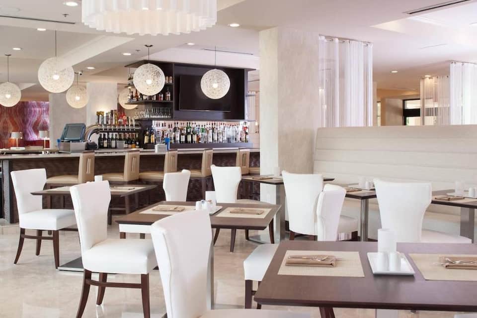 Modern restaurant interior with white chairs, dark tables, pendant globe lights, and full bar