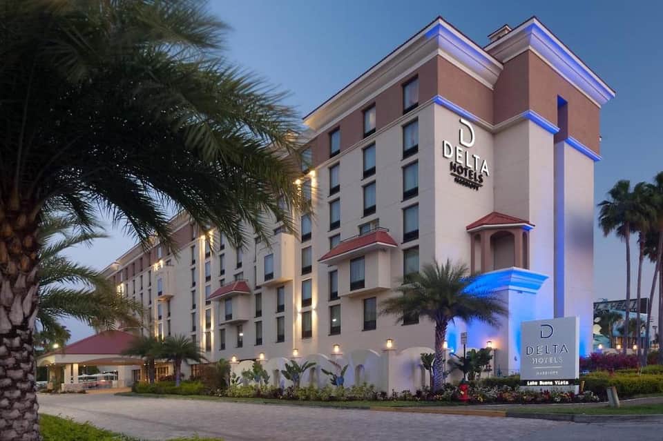 Delta Hotels building at dusk with illuminated blue accent lighting, palm trees, and landscaped grounds