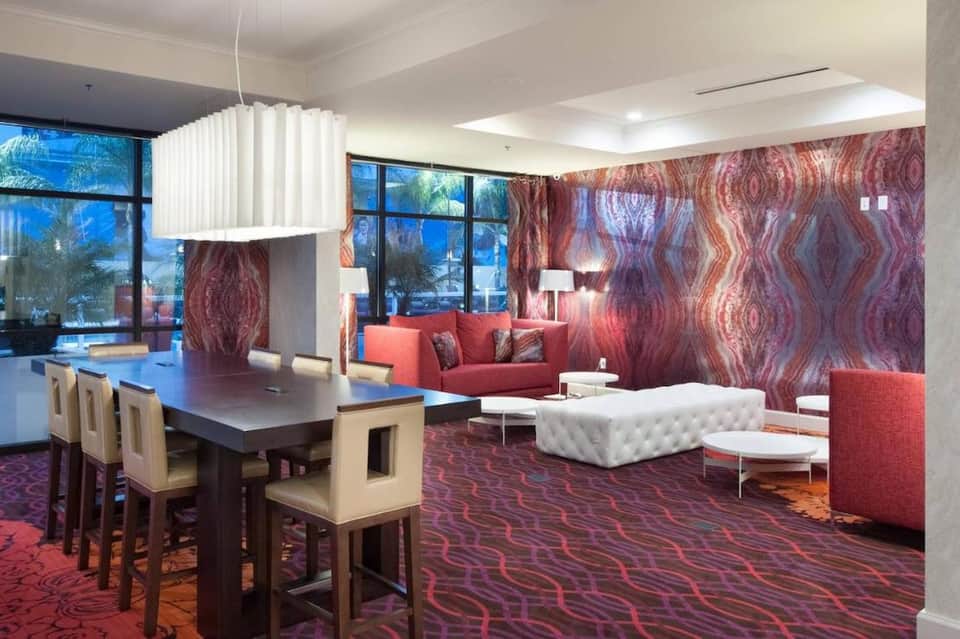 Modern hotel suite with red accent wallpaper, dining area, living space, and contemporary furnishings