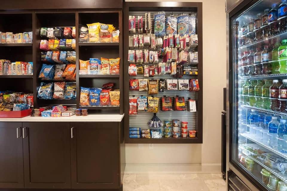 Hotel convenience shop displaying packaged snacks, beverages, and refrigerated items on shelves and coolers.