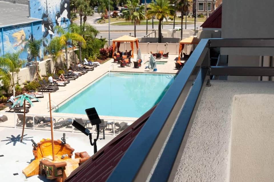 Rooftop pool deck with lounge chairs, umbrellas, and city views with palm trees