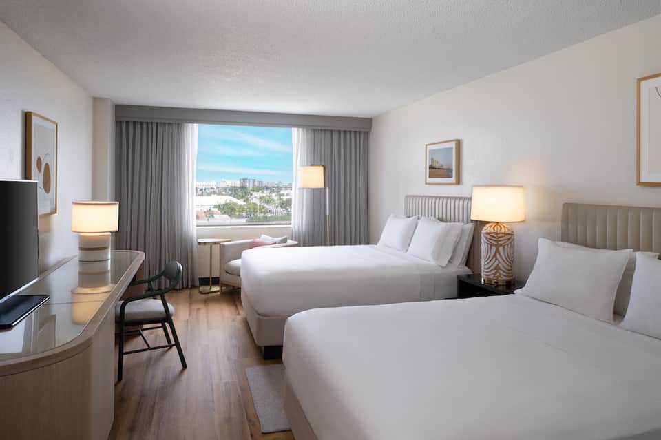 Modern hotel room with two queen beds, city view, desk, and contemporary furnishings