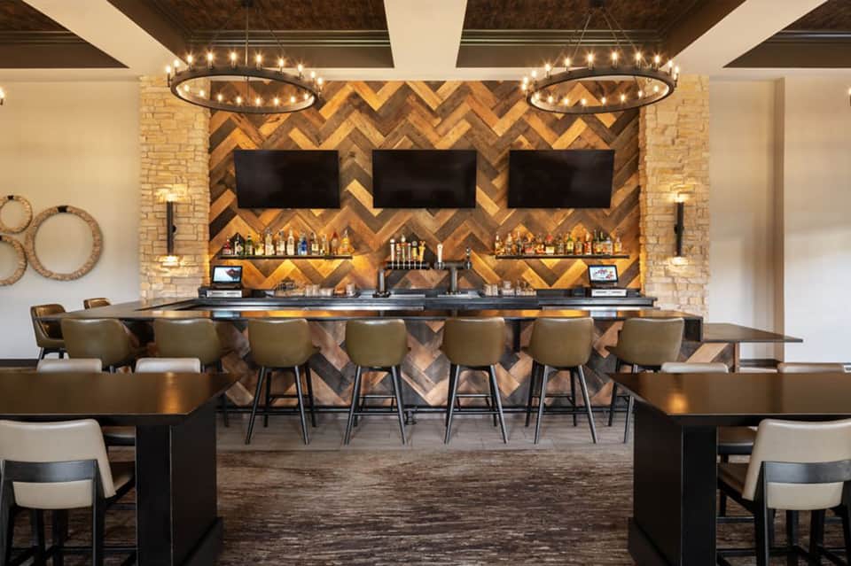 Elegant indoor bar with herringbone wood wall, circular pendant lights, and bar seating