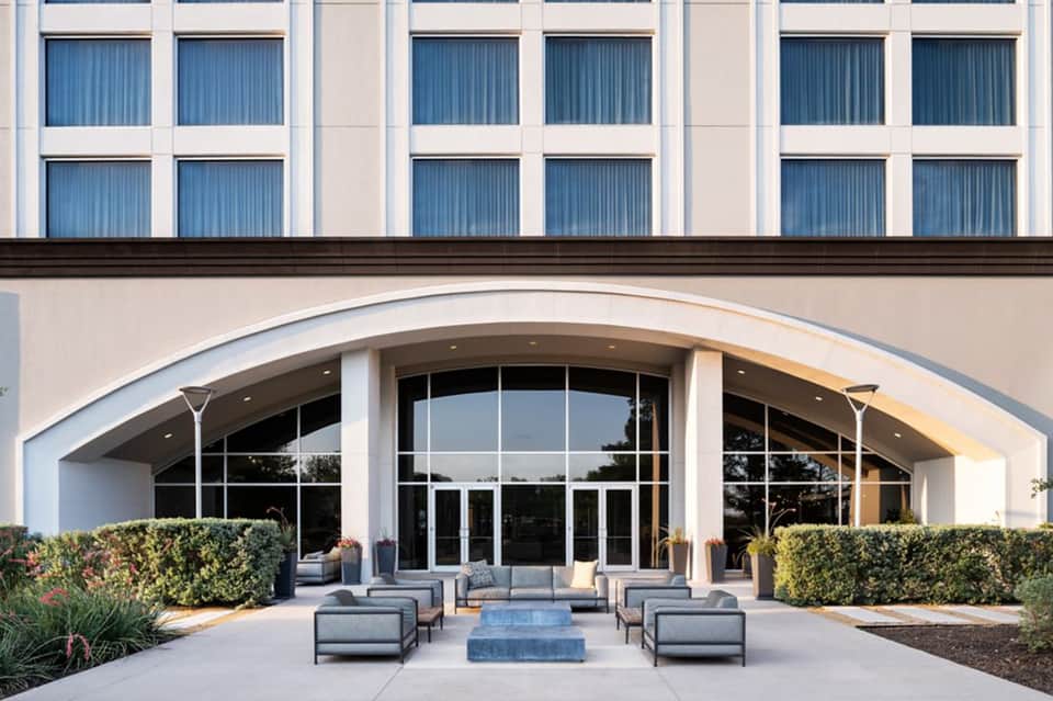 Contemporary hotel exterior entrance with curved architecture, glass doors, and modern lounge seating