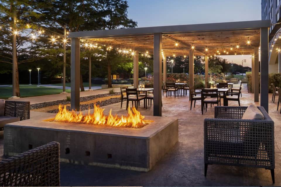 Covered patio with fireplace, dining tables, string lights, and lawn area at dusk