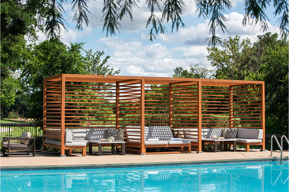 Wooden pergola structure with horizontal slats providing shade over outdoor seating by the pool