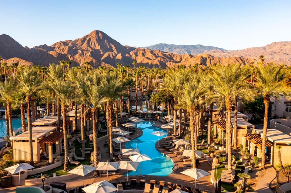 Desert resort with blue lagoon-style pool surrounded by palm trees and mountain backdrop