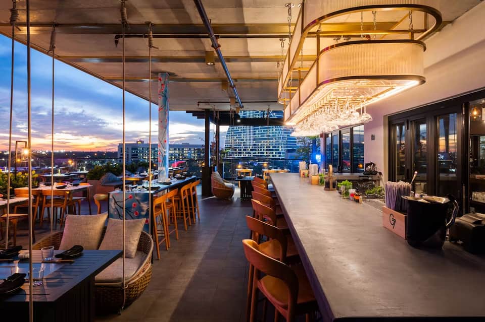 Contemporary rooftop restaurant and bar with floor-to-ceiling windows overlooking city skyline at dusk