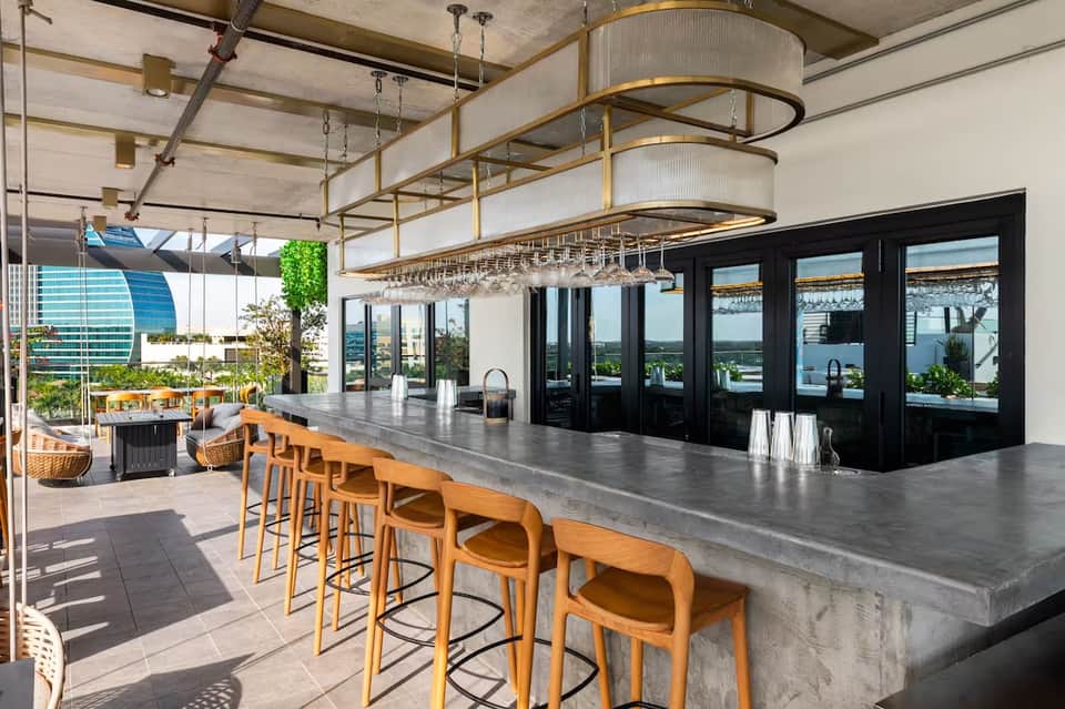 Modern rooftop bar with concrete countertop, wooden stools, pendant lighting, and panoramic waterfront views