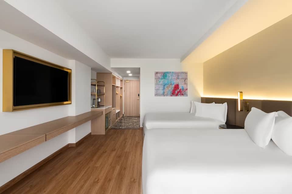 Modern hotel room with two queen beds, flat-screen TV, wood accents, and ambient lighting