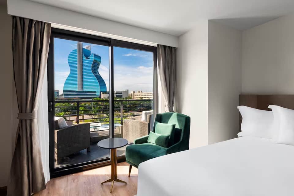 Modern hotel room with balcony view of guitar-shaped building and city skyline