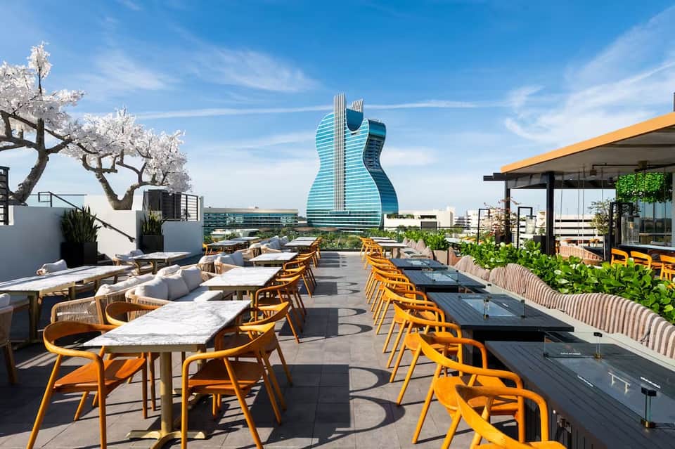 Modern rooftop restaurant with orange chairs, guitar-shaped building in background